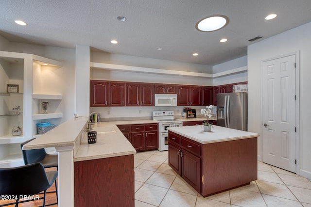 kitchen featuring light tile patterned flooring, white appliances, sink, a breakfast bar, and kitchen peninsula