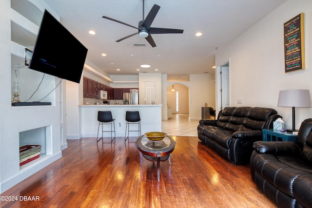 living room featuring built in features, wood-type flooring, ceiling fan, and a textured ceiling