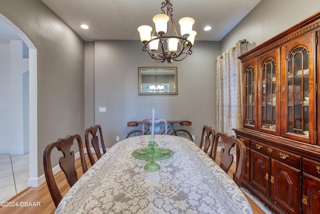 dining area with light wood-type flooring, a notable chandelier, and a textured ceiling