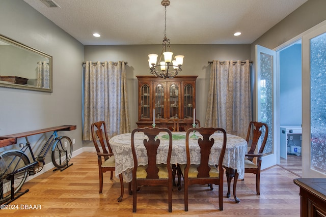 dining space with a textured ceiling, light hardwood / wood-style floors, and a chandelier