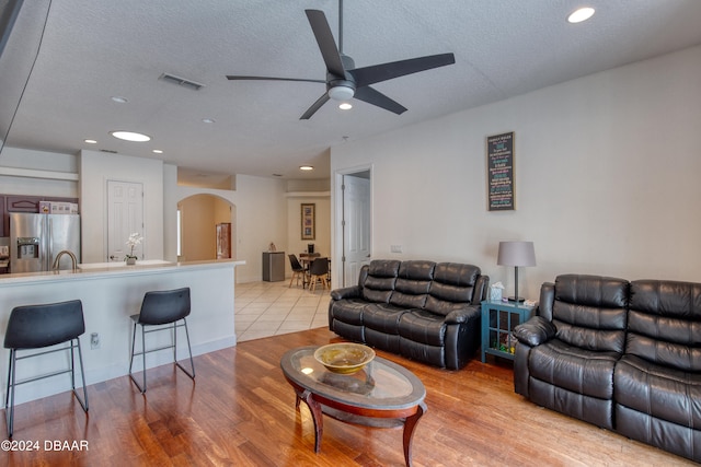 living room featuring ceiling fan, a textured ceiling, and light hardwood / wood-style floors