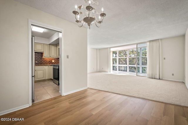 unfurnished living room featuring a notable chandelier, light hardwood / wood-style floors, and a textured ceiling