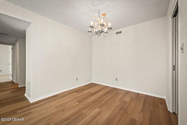 unfurnished dining area featuring a textured ceiling, a notable chandelier, and hardwood / wood-style flooring