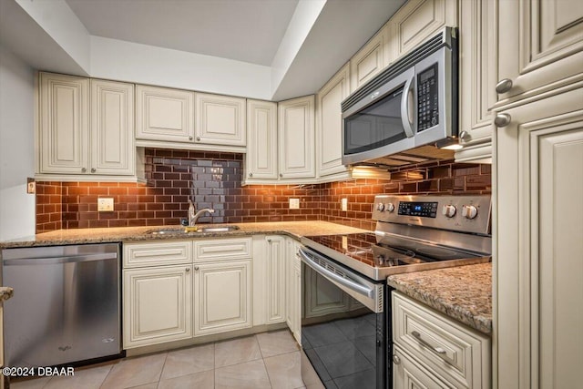 kitchen with cream cabinetry, appliances with stainless steel finishes, light stone countertops, and sink