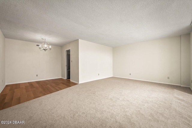 empty room featuring a textured ceiling, hardwood / wood-style flooring, and an inviting chandelier