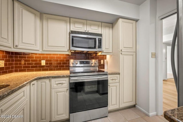 kitchen with cream cabinetry, backsplash, light stone counters, and stainless steel appliances