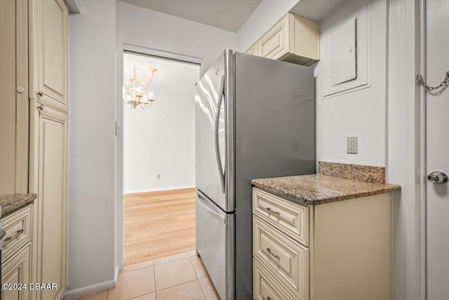 kitchen featuring stainless steel fridge, cream cabinets, stone counters, and light tile patterned flooring