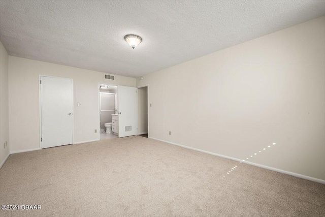 unfurnished bedroom featuring connected bathroom, light colored carpet, and a textured ceiling