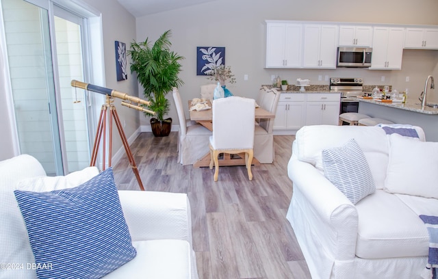 kitchen featuring light wood-type flooring, light stone counters, white cabinetry, stainless steel appliances, and baseboards