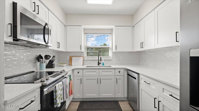 kitchen with backsplash, appliances with stainless steel finishes, white cabinetry, and a sink