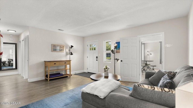 living area with baseboards, a textured ceiling, and wood finished floors