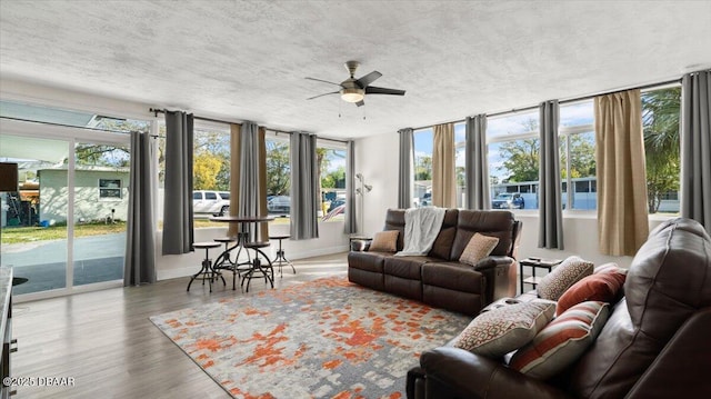 living area featuring baseboards, a textured ceiling, wood finished floors, and a ceiling fan