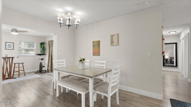 dining room with light wood finished floors, ceiling fan with notable chandelier, and baseboards