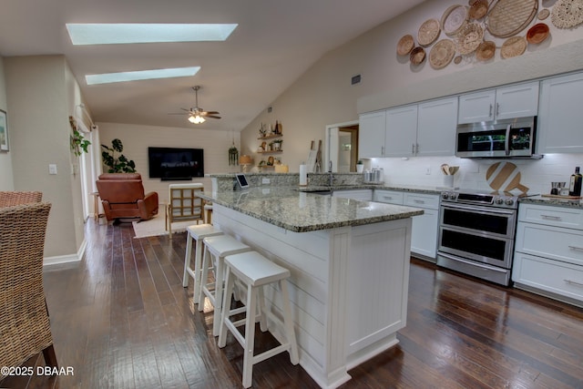 kitchen with appliances with stainless steel finishes, a breakfast bar area, white cabinets, and dark hardwood / wood-style flooring