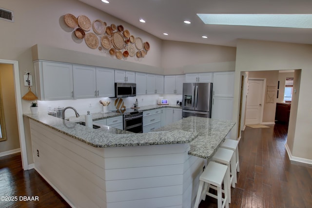 kitchen featuring white cabinetry, a breakfast bar area, light stone counters, kitchen peninsula, and stainless steel appliances