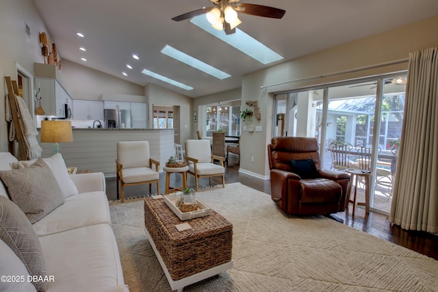 living room featuring hardwood / wood-style floors, a skylight, high vaulted ceiling, and ceiling fan