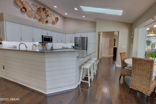 kitchen featuring white cabinetry, appliances with stainless steel finishes, vaulted ceiling with skylight, and light stone counters