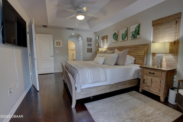 bedroom featuring ceiling fan, connected bathroom, a tray ceiling, dark hardwood / wood-style flooring, and a closet