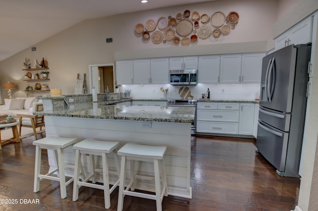 kitchen with white cabinetry, stainless steel appliances, a kitchen bar, dark hardwood / wood-style flooring, and kitchen peninsula