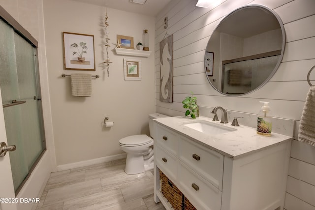 full bathroom featuring vanity, wooden walls, shower / bath combination with glass door, and toilet