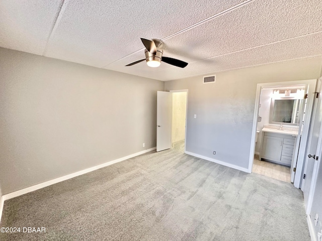 unfurnished bedroom featuring a textured ceiling, light carpet, ceiling fan, and ensuite bath