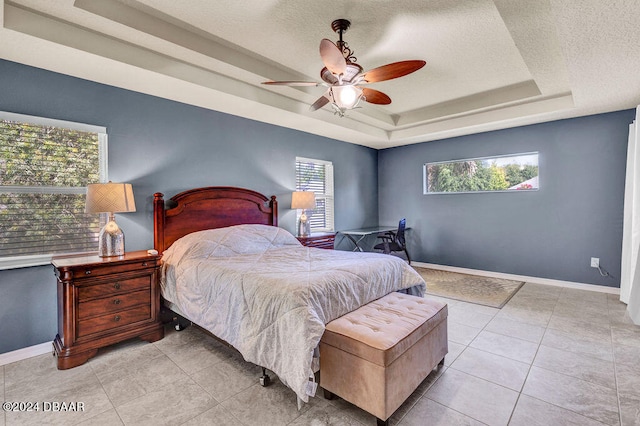 tiled bedroom with ceiling fan, multiple windows, a tray ceiling, and a textured ceiling