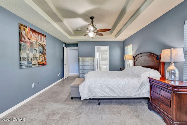 bedroom with ceiling fan, ensuite bath, a tray ceiling, and a textured ceiling