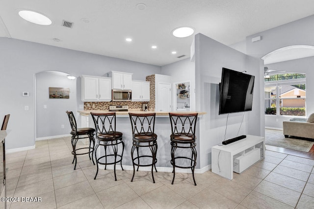 kitchen with white cabinetry, ceiling fan, stainless steel appliances, backsplash, and a breakfast bar