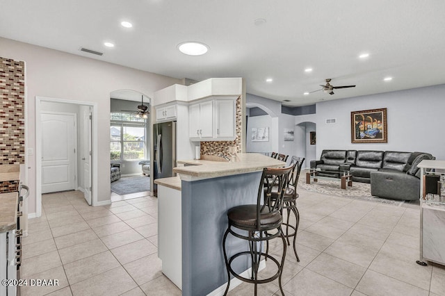 kitchen featuring white cabinetry, kitchen peninsula, ceiling fan, light tile patterned flooring, and a breakfast bar