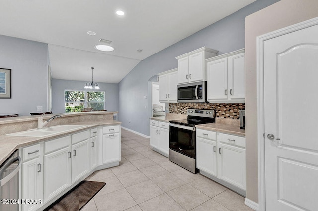 kitchen featuring stainless steel appliances, decorative light fixtures, lofted ceiling, white cabinets, and sink