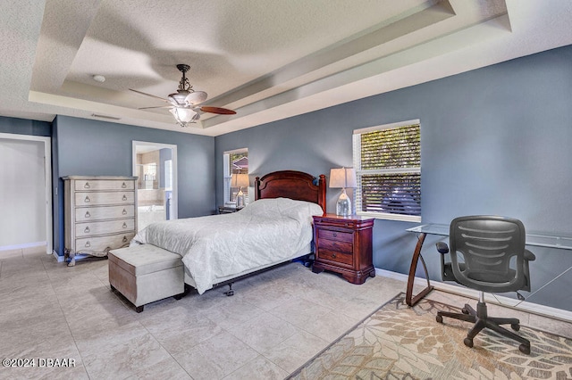 bedroom with ceiling fan, a tray ceiling, and ensuite bath