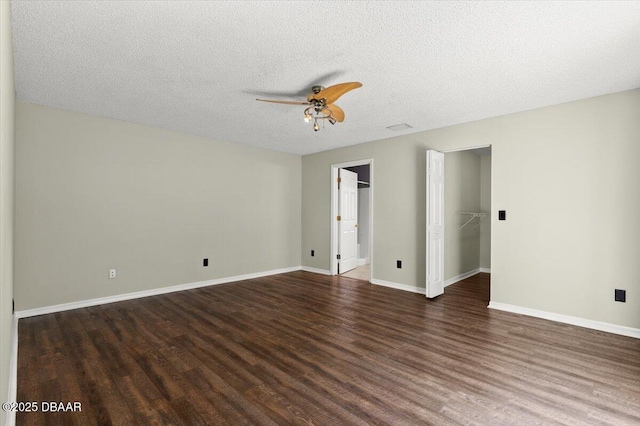 unfurnished bedroom featuring a walk in closet, a ceiling fan, a textured ceiling, wood finished floors, and baseboards