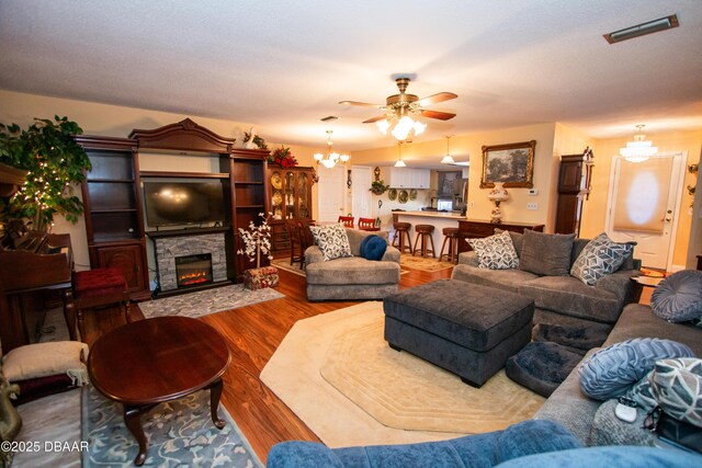 living area with ceiling fan with notable chandelier, visible vents, a fireplace, and wood finished floors