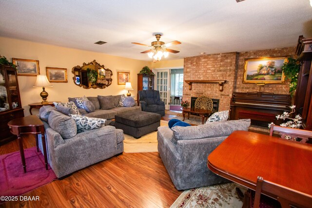 living room with ceiling fan, visible vents, a fireplace, and wood finished floors