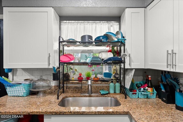 kitchen featuring white cabinets, sink, light stone counters, and backsplash