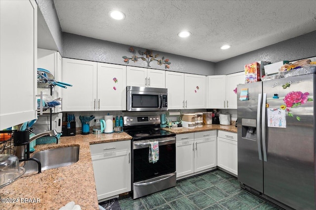 kitchen featuring light stone counters, white cabinets, a textured ceiling, sink, and appliances with stainless steel finishes