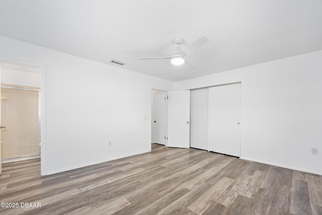 unfurnished bedroom featuring ceiling fan, ensuite bath, wood finished floors, visible vents, and a closet