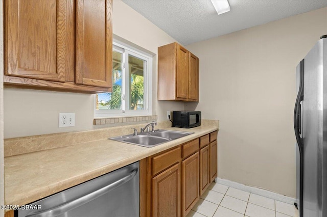 kitchen with sink, light tile patterned floors, stainless steel appliances, and a textured ceiling