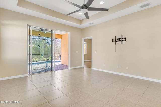 tiled spare room featuring a raised ceiling and ceiling fan