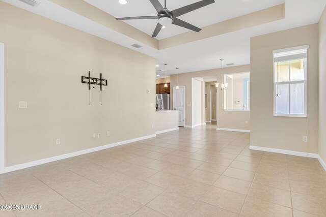 tiled spare room featuring a raised ceiling and ceiling fan with notable chandelier