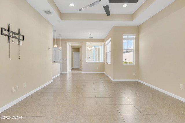 tiled spare room featuring a tray ceiling and ceiling fan with notable chandelier