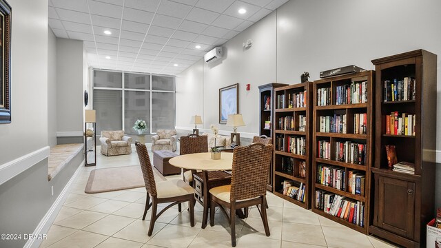 tiled dining space with a wall mounted AC, a drop ceiling, and a high ceiling