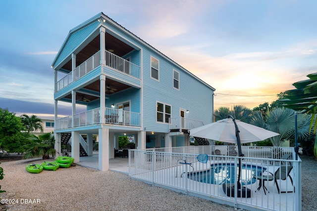 back house at dusk featuring a balcony, a patio, and a fenced in pool