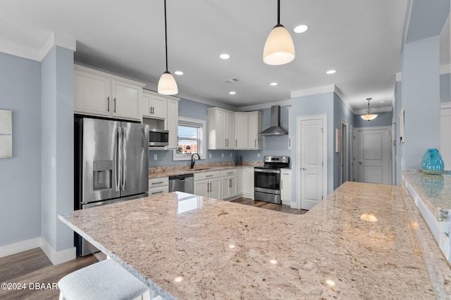 kitchen featuring wall chimney range hood, white cabinetry, decorative light fixtures, and appliances with stainless steel finishes