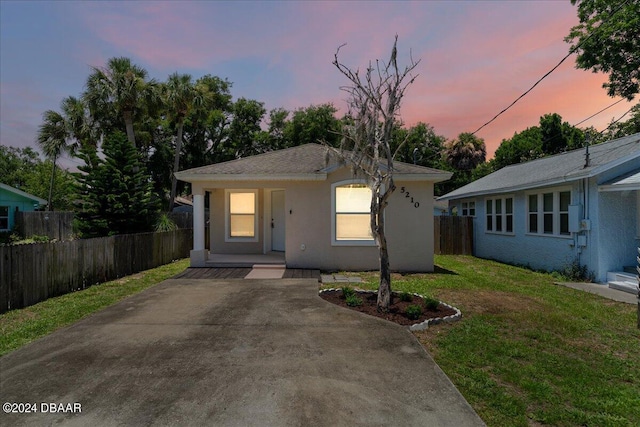 bungalow-style house featuring a porch, a yard, fence, and stucco siding