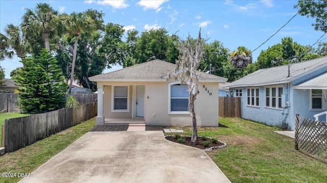 bungalow-style house with stucco siding, a shingled roof, a front lawn, and fence