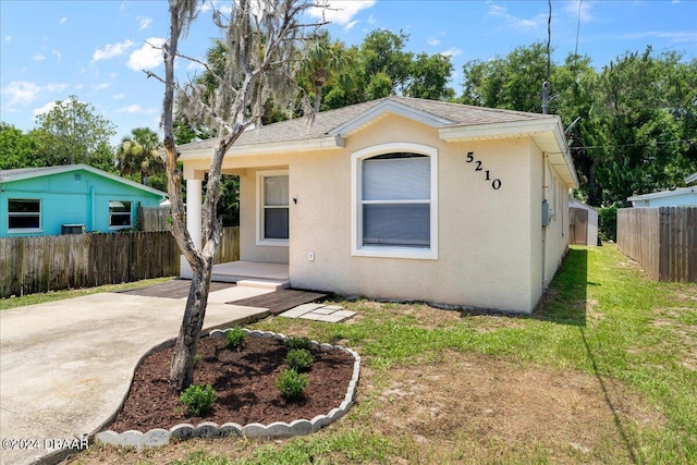 bungalow featuring a front yard, fence, roof with shingles, and stucco siding