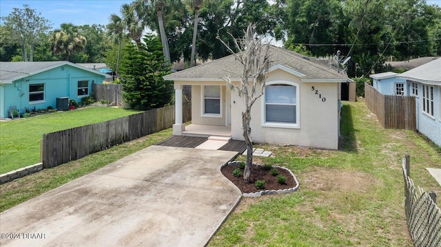 bungalow with stucco siding, central AC unit, a front yard, fence, and driveway