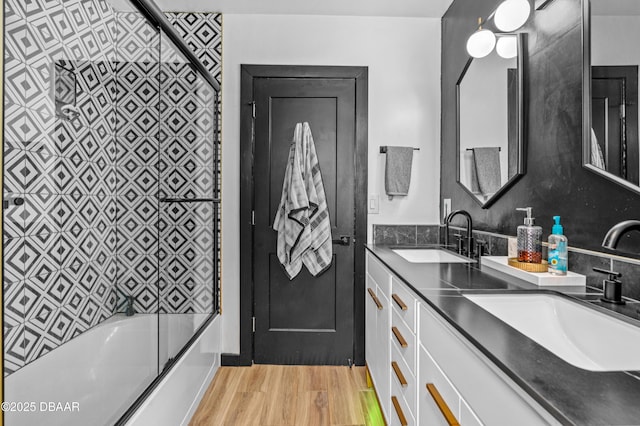 bathroom featuring wood finished floors, shower / bath combination with glass door, and double vanity