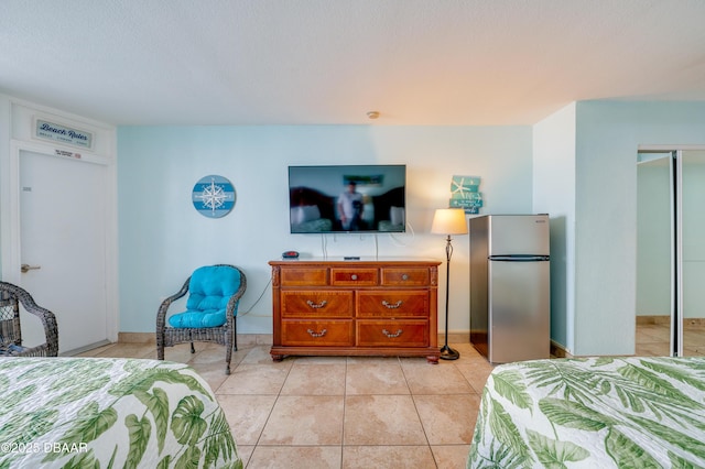 bedroom with light tile patterned floors, stainless steel fridge, and a closet